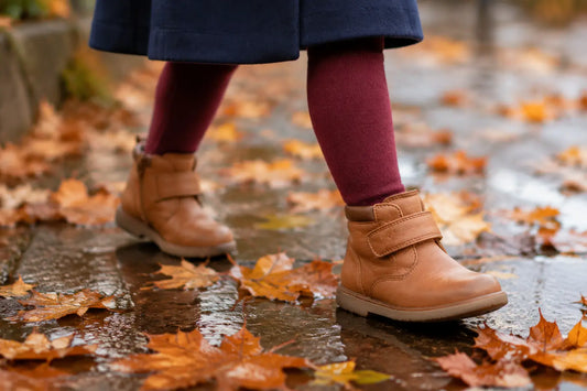 Petite fille en bottines en cuir camel à scratch marchant sur un trottoir mouillé couvert de feuilles d'automne