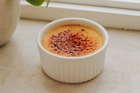 Crème brûlée enceinte en ramequin, sur plan de travail de cuisine, lumière naturelle douce près d’une fenêtre.