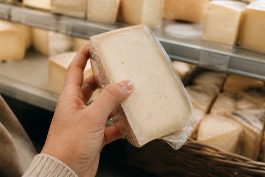 Main dans le rayon fromages, lisant une étiquette, pour un article sur la mimolette enceinte.