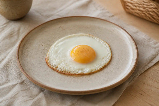 Oeuf au plat enceinte sur assiette en céramique, gros plan lumineux sur table de cuisine, style éditorial naturel