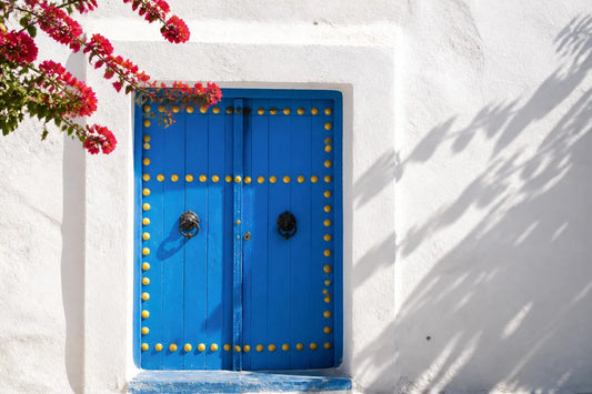 Porte tunisienne traditionnelle en bois bleu cloutée de jaune dans un mur blanchi à la chaux